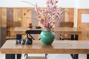 A wooden table with a green vase containing pink flowers, a teapot, and a cup.