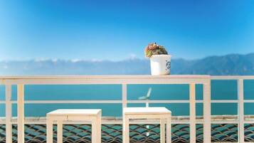 A balcony with a white railing, two white chairs, and a potted plant.