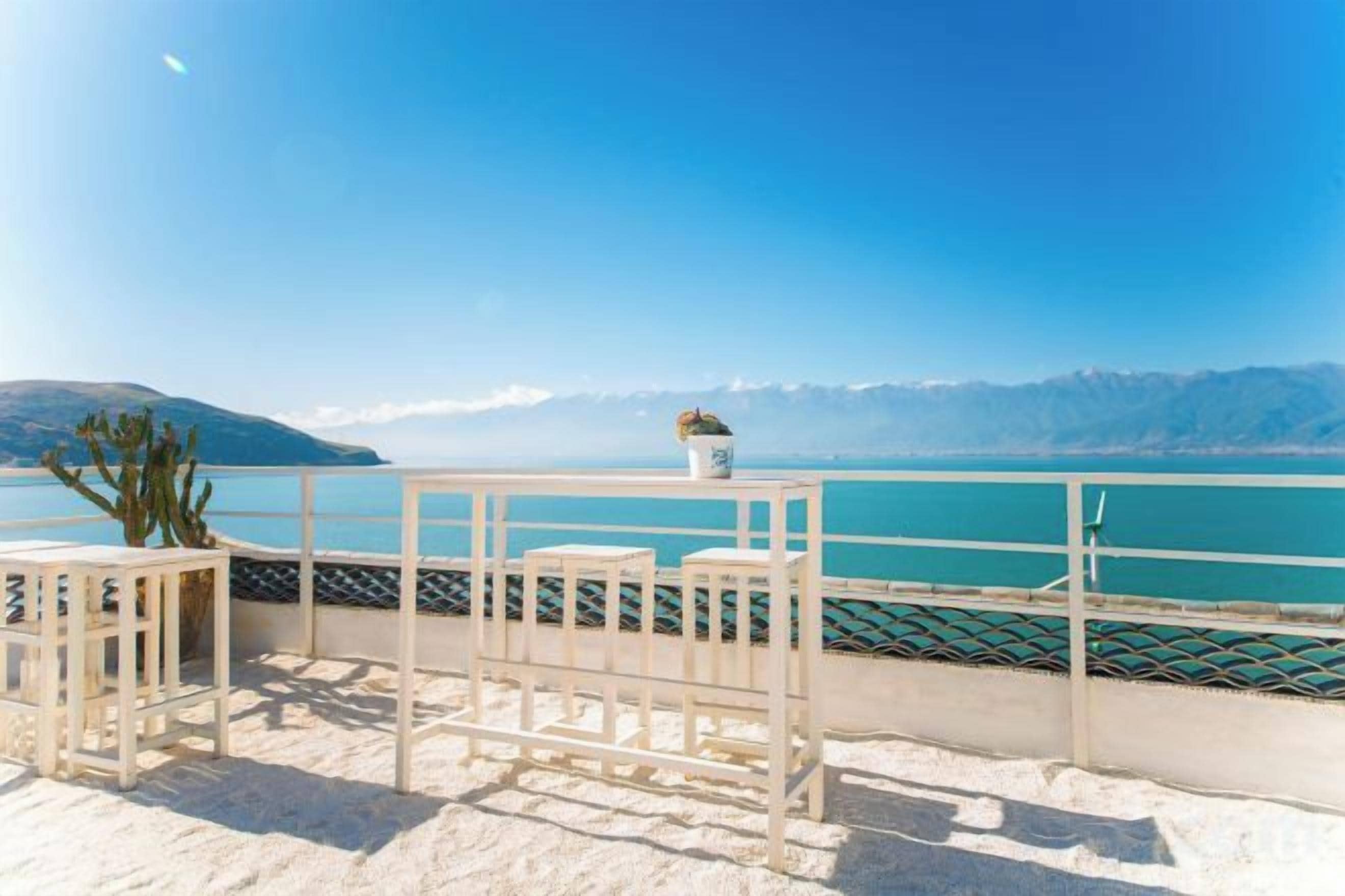 Una terraza con mesa y sillas, con vistas a un cuerpo de agua y montañas.