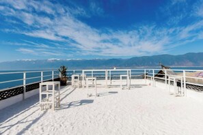 Um terraço à beira-mar com guarda branco, planta em vaso e vista para o mar e montanhas.
