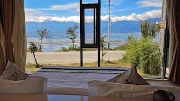 A room with a bed facing a scenic view of a lake and mountains.