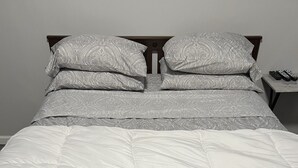 A bed with a white quilt and patterned pillows, a nightstand with a remote control, and a dark wooden headboard.