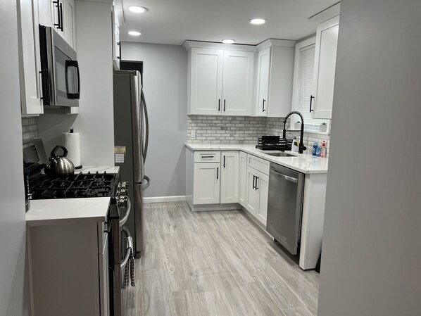 A modern kitchen with white cabinets, a stainless steel refrigerator, a gas stove, and a dishwasher.
