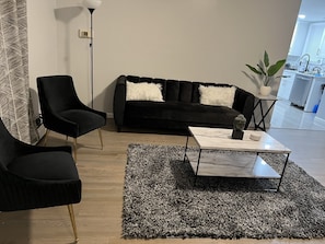 A modern living room with a black sofa, two black armchairs, a marble coffee table, and a shaggy rug.