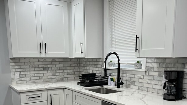 A modern kitchen with white cabinets, a stainless steel dishwasher, and a marble countertop.