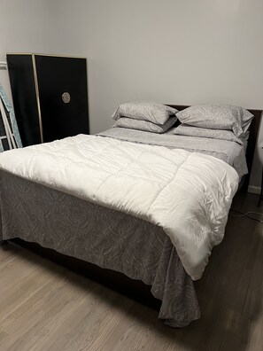 A bed with a patterned bedspread and pillows, a wardrobe, and a wooden floor.