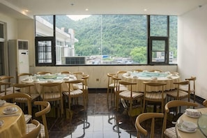Uma área de refeições com mesas e cadeiras redondas, janelas amplas com vista para uma paisagem montanhosa e um design de interiores moderno.