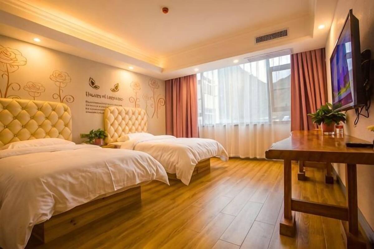 Habitación de hotel con dos camas, piso de madera, televisor y un ventanal decorado con motivos florales.