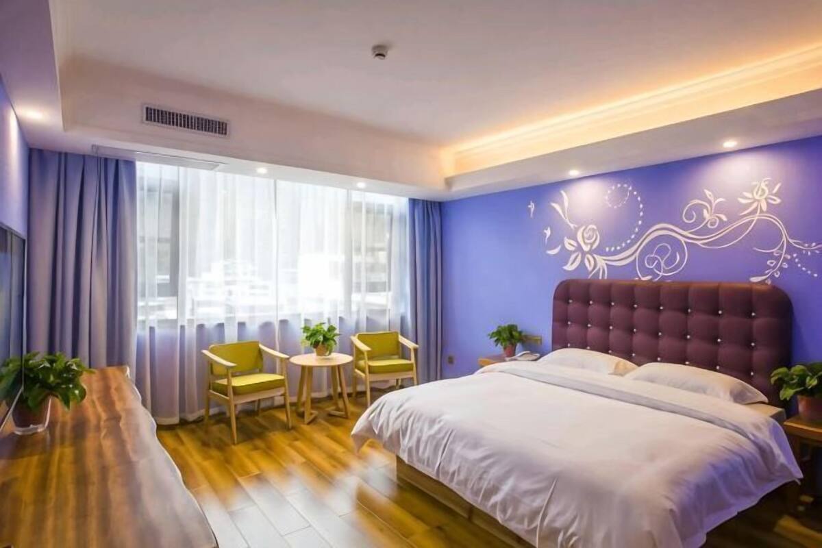 Un dormitorio con una cama grande, una mesita, dos sillas y una ventana con cortinas.