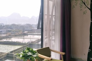A room with a view of a river and mountains, a chair, and a potted plant. - Tao Flute Hotel (Guilin)