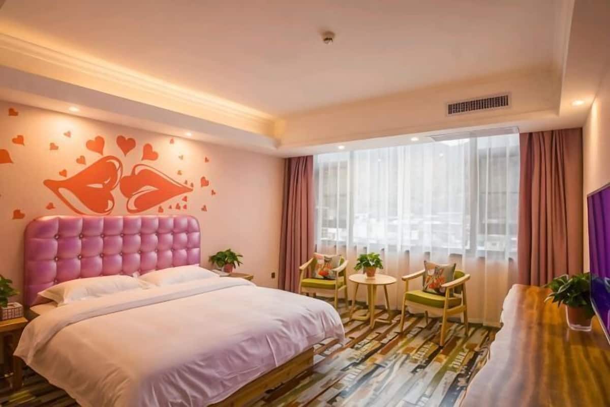 Ein Hotelzimmer mit einem großen Bett, einem kleinen Tisch mit Stühlen, einem Fenster mit Vorhängen und einer Wand mit Herzdekorationen.