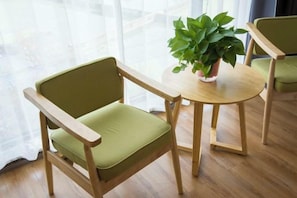 Una habitación con piso de madera, una silla verde con apoyabrazos de madera y una mesa redonda de madera con una planta en maceta.