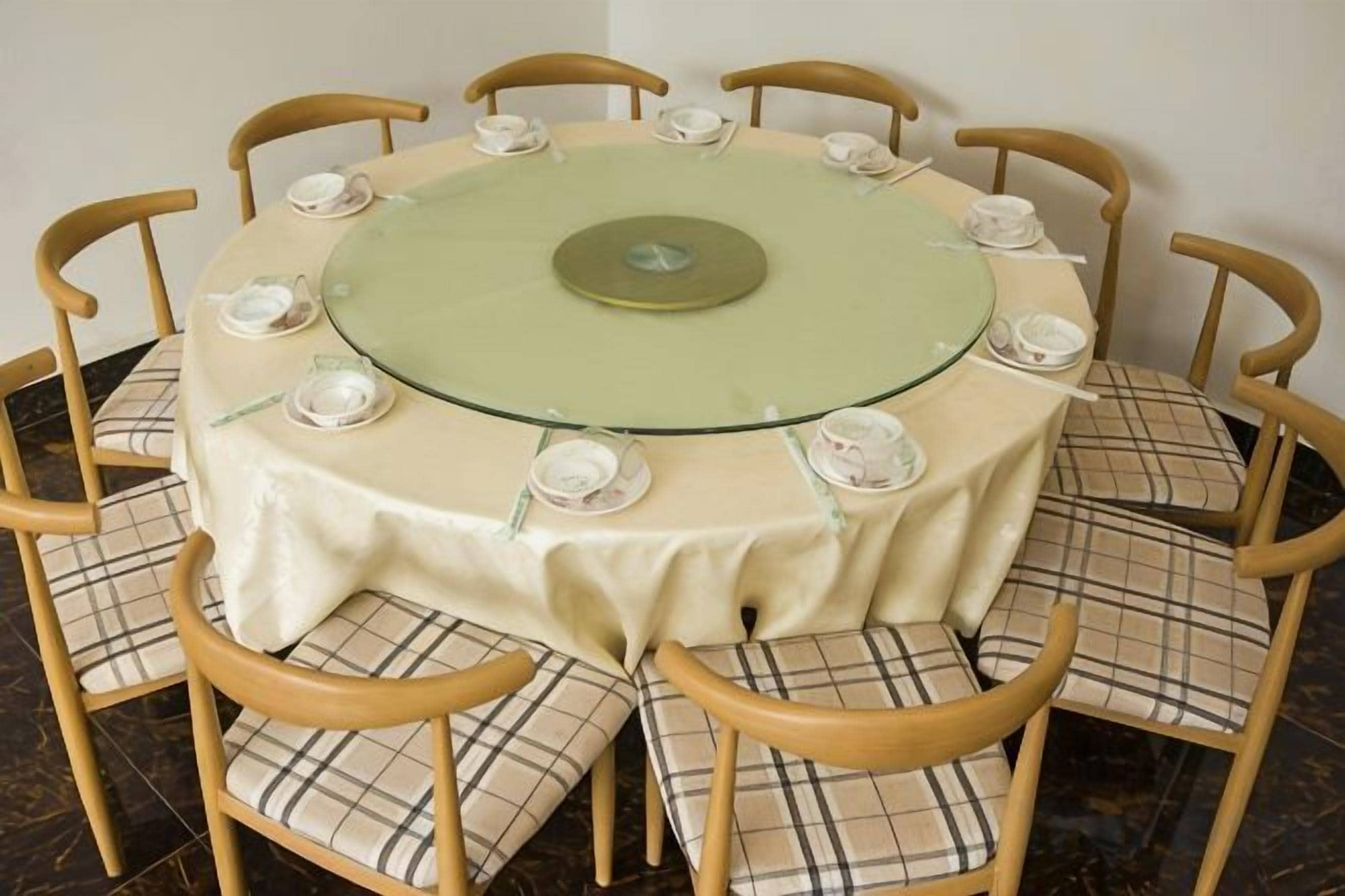 A round table with a green glass top surrounded by six chairs with plaid cushions.