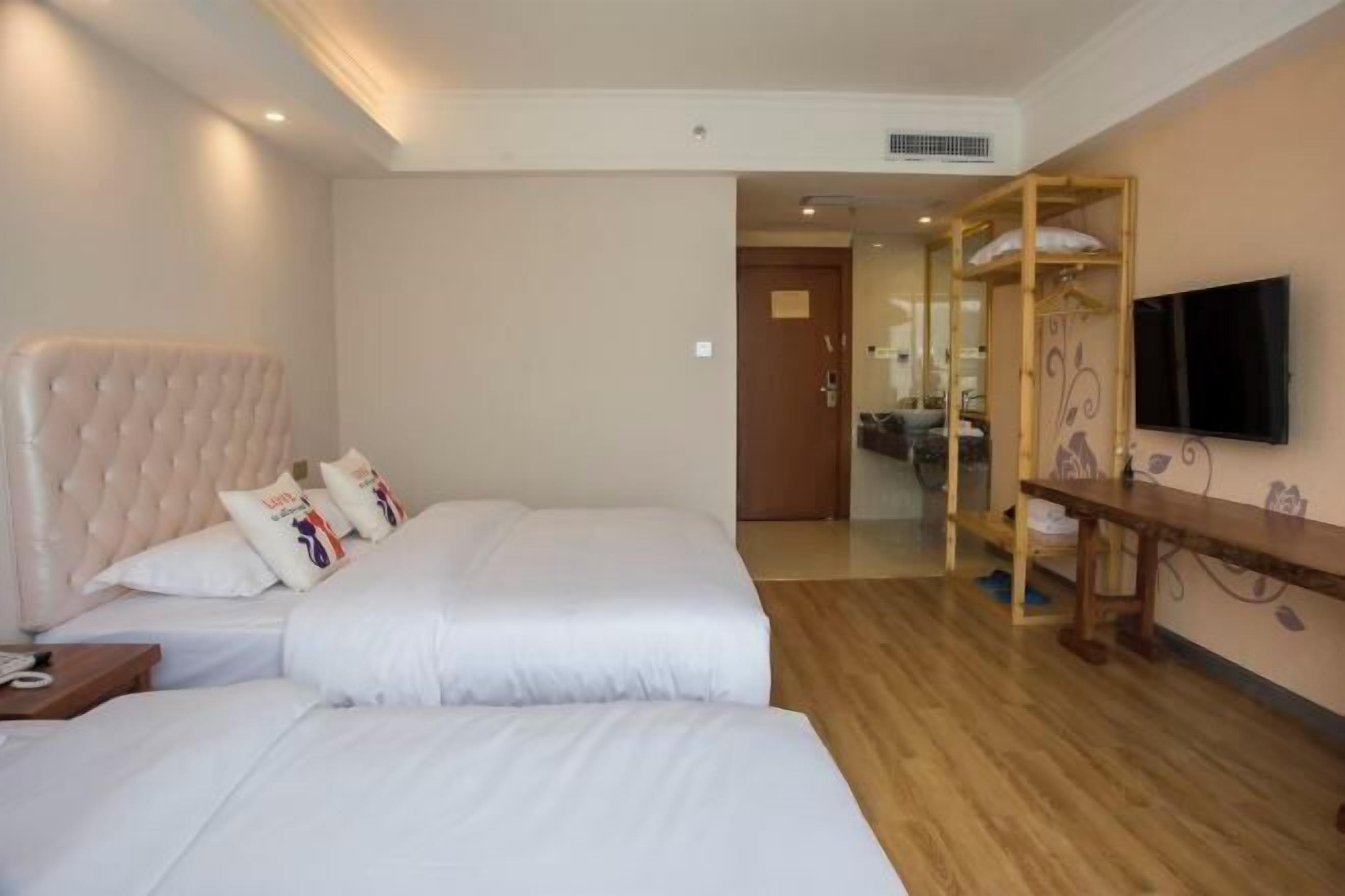 Een hotelkamer met twee bedden, een houten vloer, een aan de muur bevestigde televisie en een spiegel.