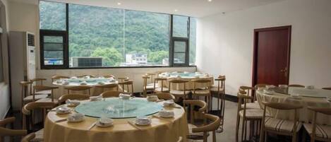 Un comedor con mesas redondas, sillas y un ventanal con vistas a la montaña.