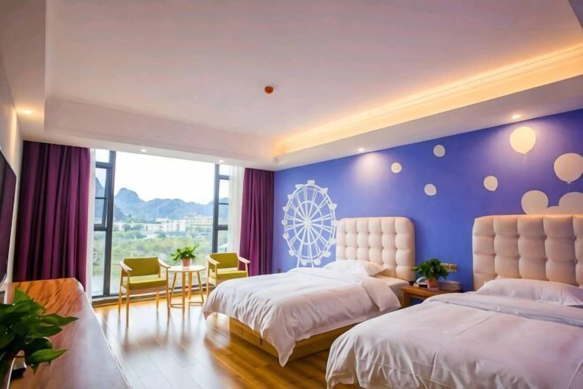 Ein Hotelzimmer mit zwei Betten, einem großen Fenster, Blick auf die Stadt und einer Wandverzierungen.