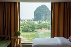 A hotel room with a bed, a small round table with a plant, and a window with curtains. - Tao Flute Hotel (Guilin)