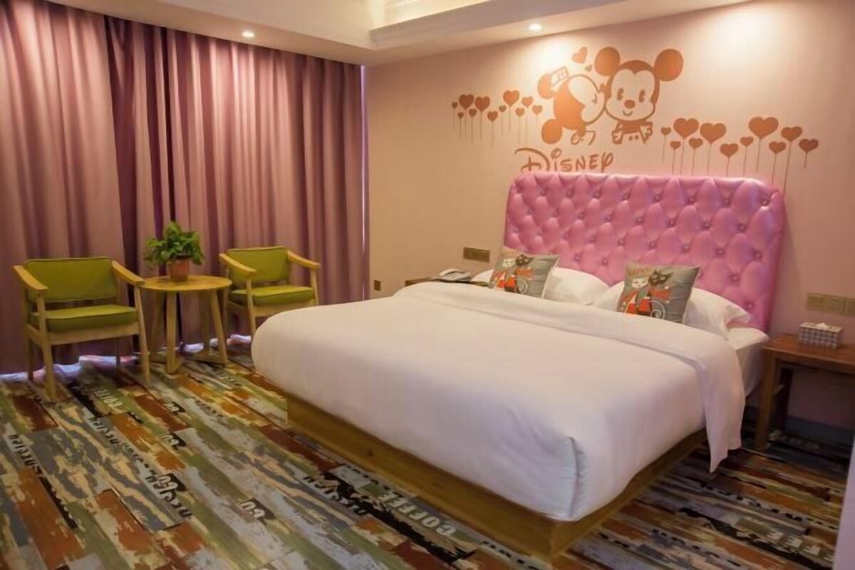 A hotel room with a large bed, a small table with chairs, a potted plant, and a wall with Disney-themed decorations.