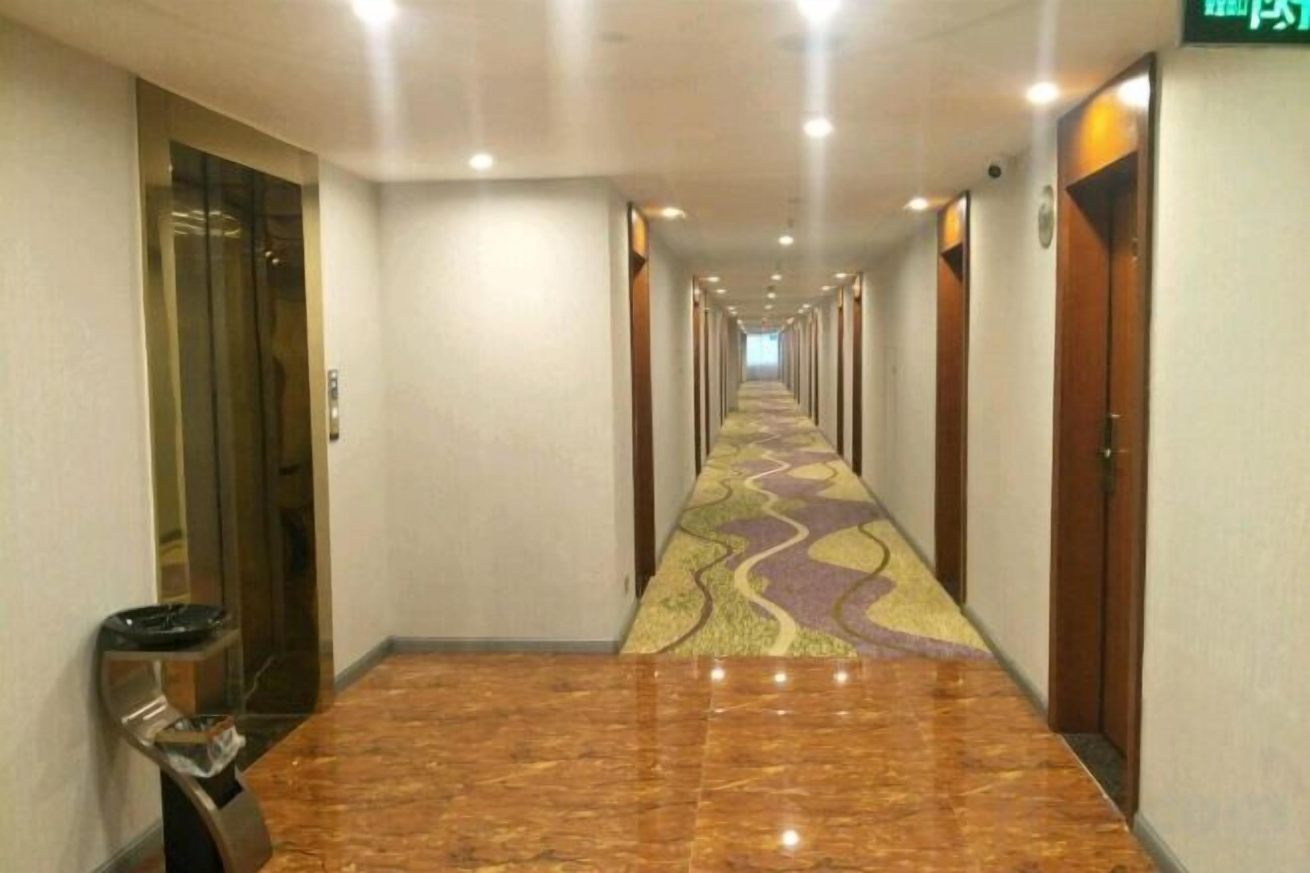Un couloir d’hôtel avec un tapis à motifs, des portes des deux côtés et une poubelle sur la gauche.