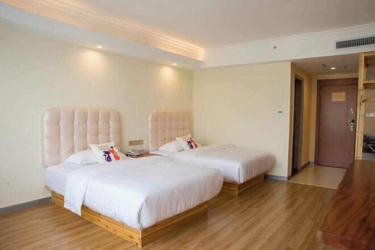 A hotel room with two beds, wooden flooring, and a door leading to another room.