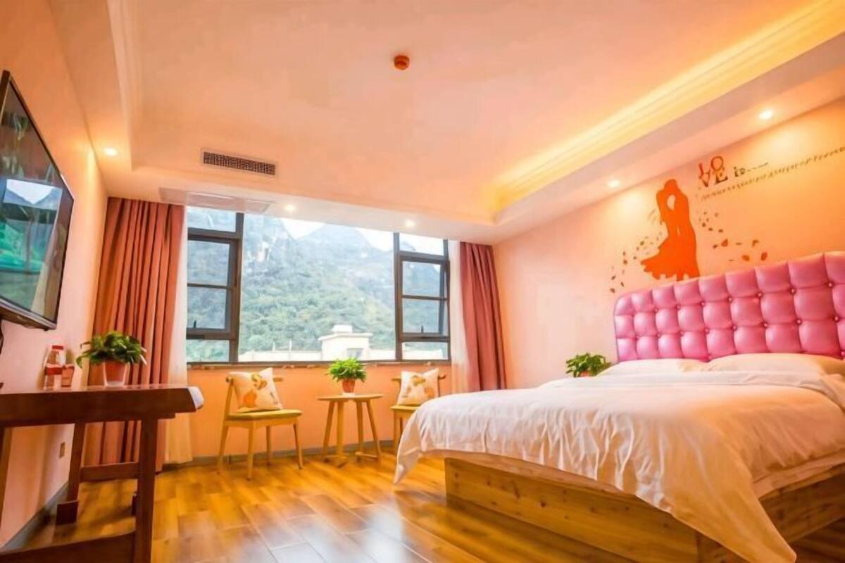 Un dormitorio con cama, escritorio, dos sillas, ventana con vistas y decoración en la pared.
