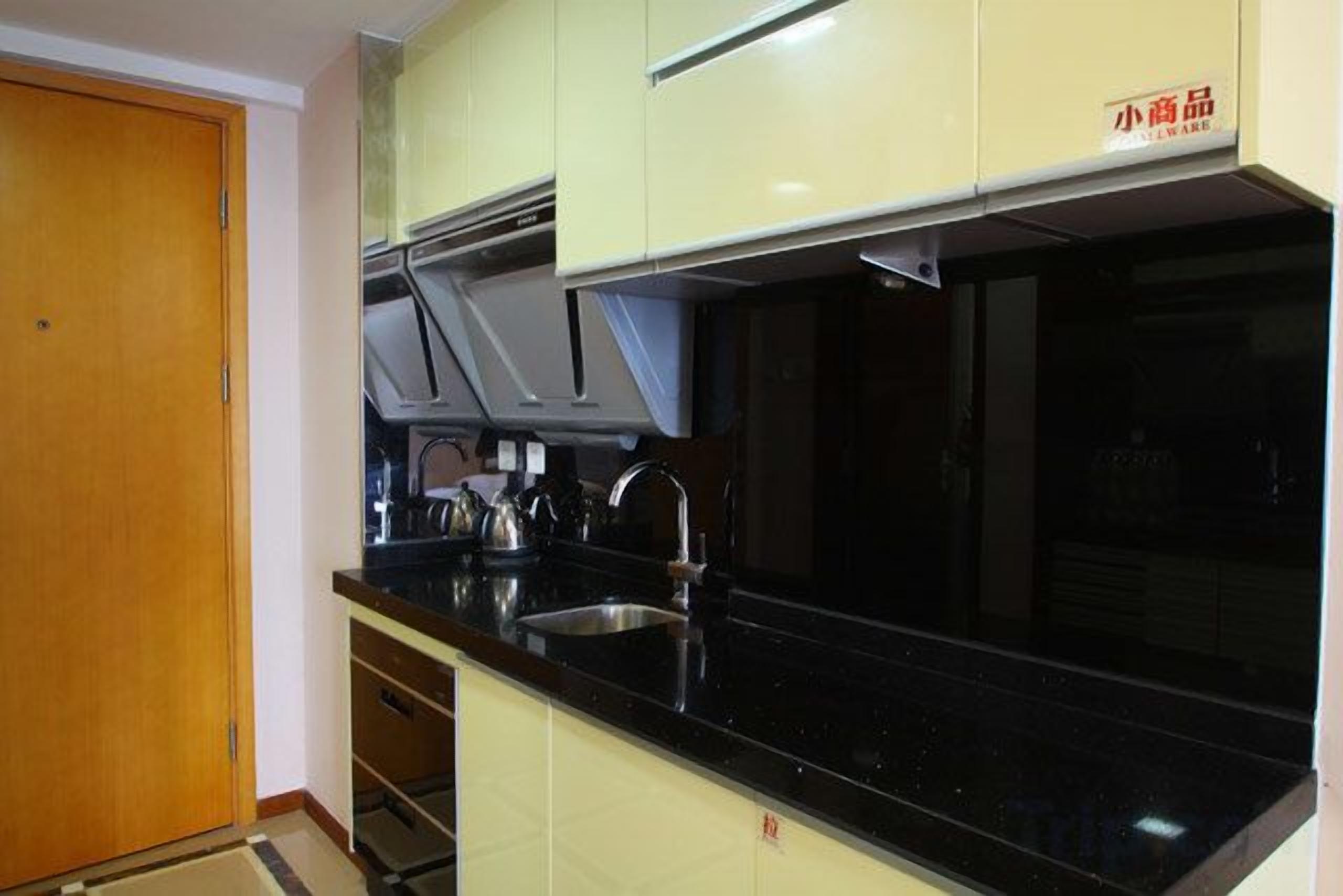 Una cocina con encimera negra, pileta de acero inoxidable y alacenas de color claro.