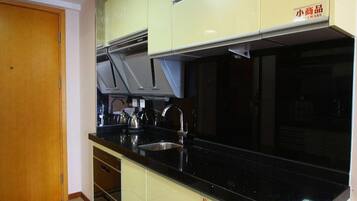 Una cocina con encimera negra, pileta de acero inoxidable y alacenas de color claro.
