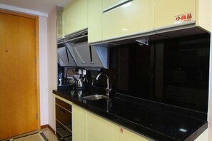 A kitchen with a black countertop, stainless steel sink, and light-colored cabinets. - roomme hospitality (Foshan)