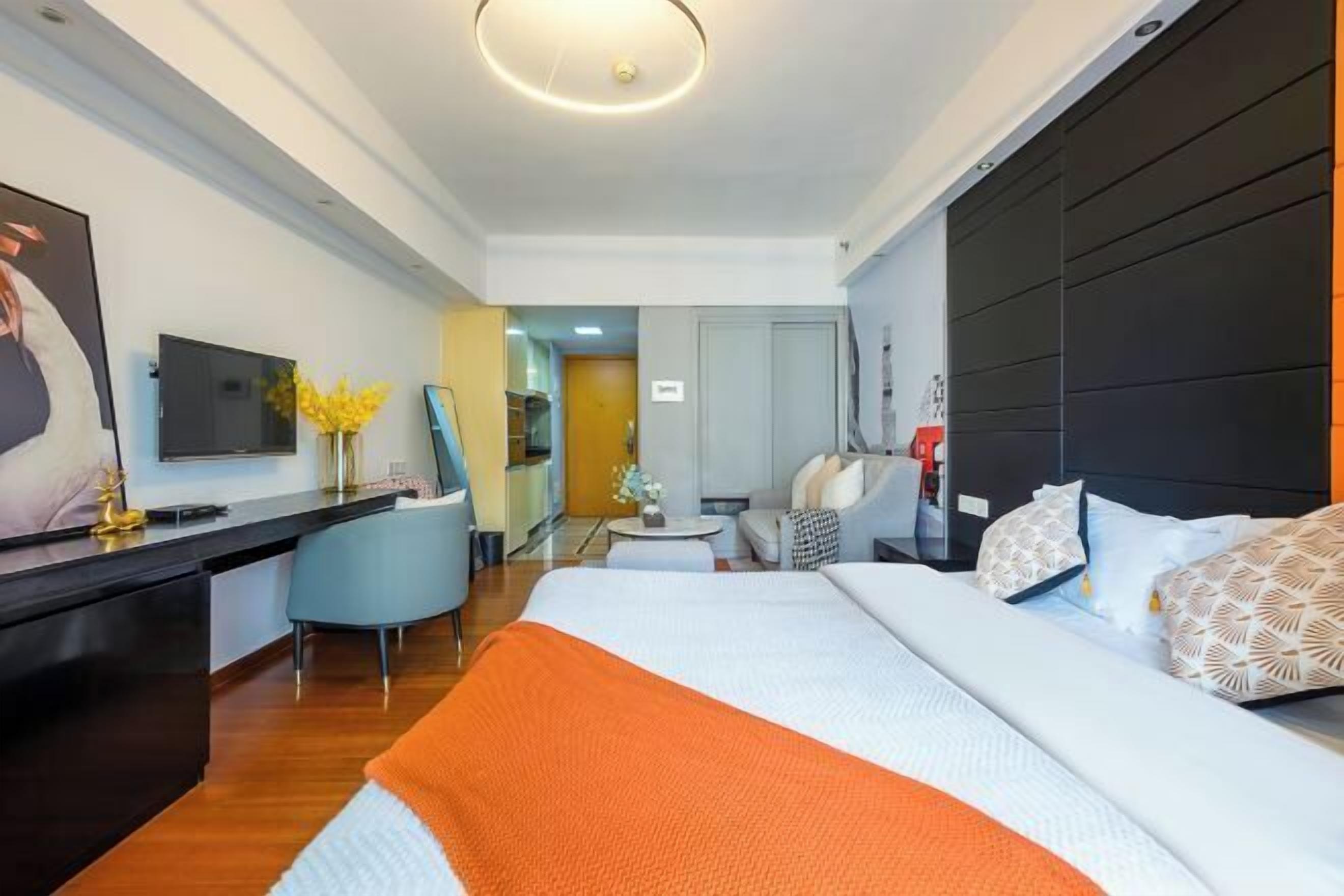 Habitación de hotel moderna con una cama grande, un escritorio con televisor de pantalla plana, un rincón de descanso con una silla y una mesita, y otra habitación visible a través de una puerta abierta.