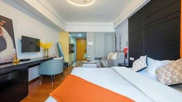 Habitación de hotel moderna con una cama grande, un escritorio con televisor de pantalla plana, un rincón de descanso con una silla y una mesita, y otra habitación visible a través de una puerta abierta.
