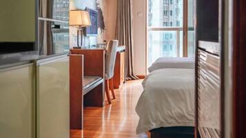 Habitación de hotel con cama, escritorio, silla y ventana con vistas a la ciudad.
