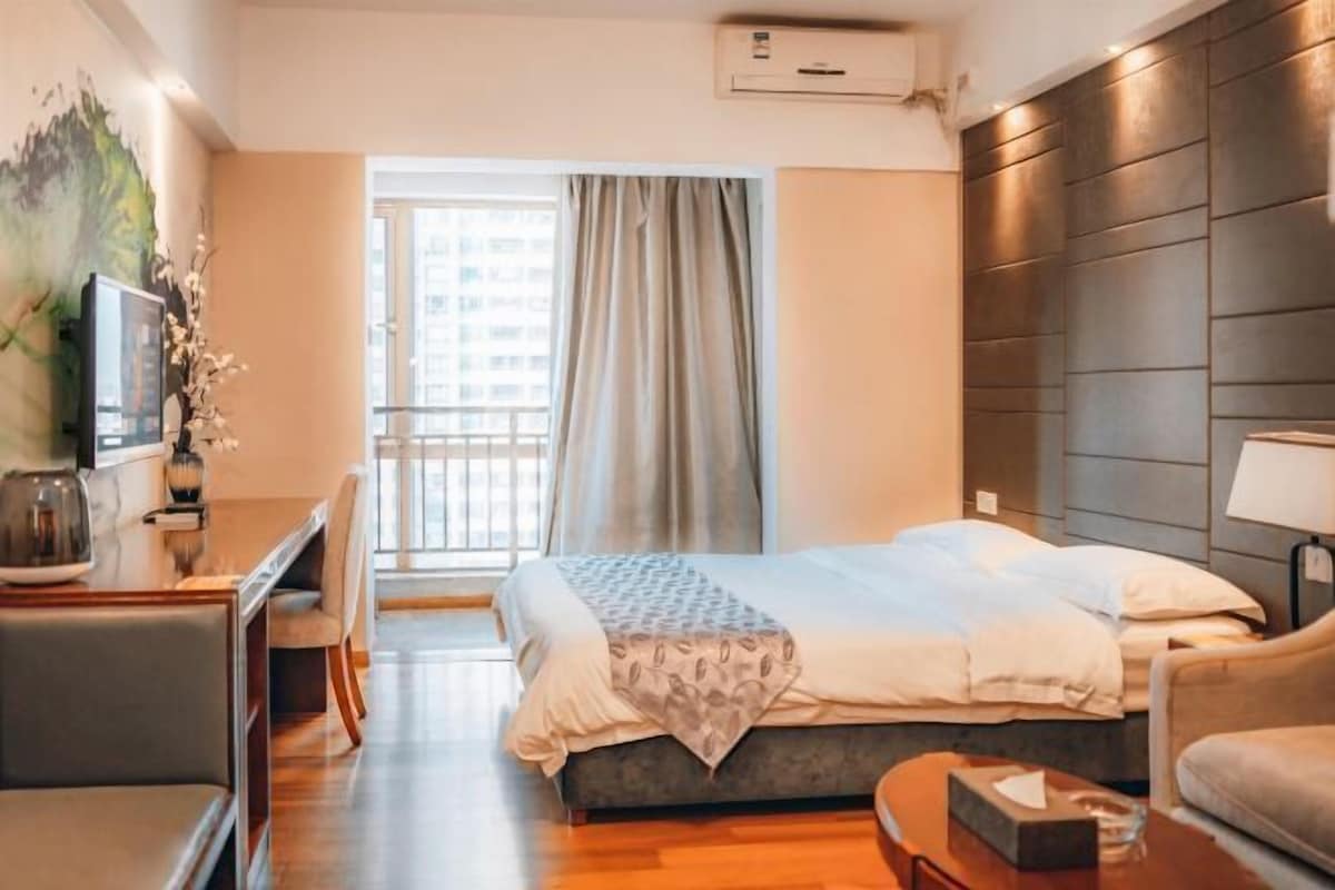 A modern hotel room with a bed, a desk, a chair, and a window with curtains.