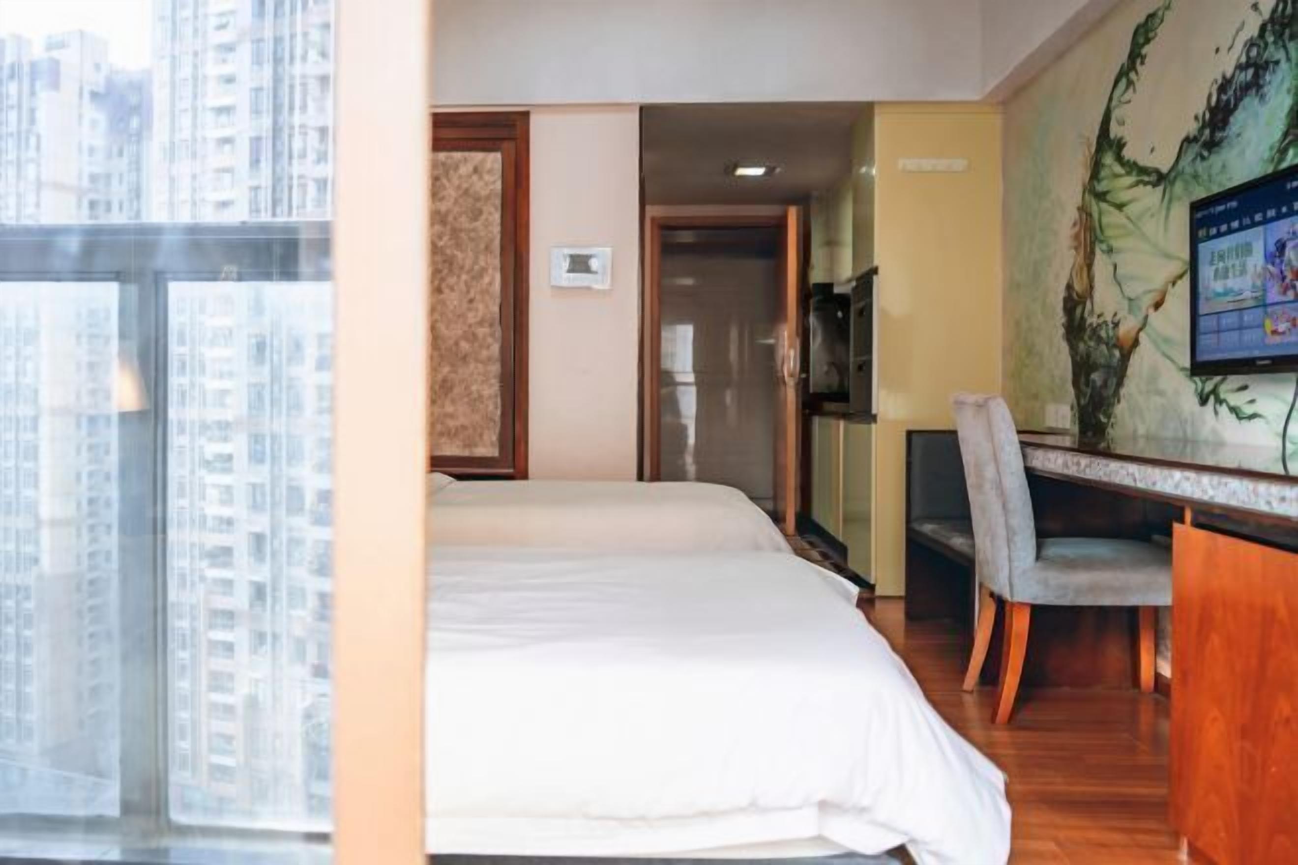 Hotelkamer met een bed, bureau, stoel, televisie en uitzicht op wolkenkrabbers.