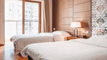 Habitación de hotel con dos camas, cabecero de madera, mesita de noche con lámpara y ventana con cortinas.