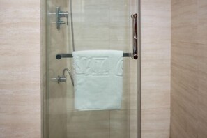 A glass-enclosed shower stall with a towel rack holding a white towel.