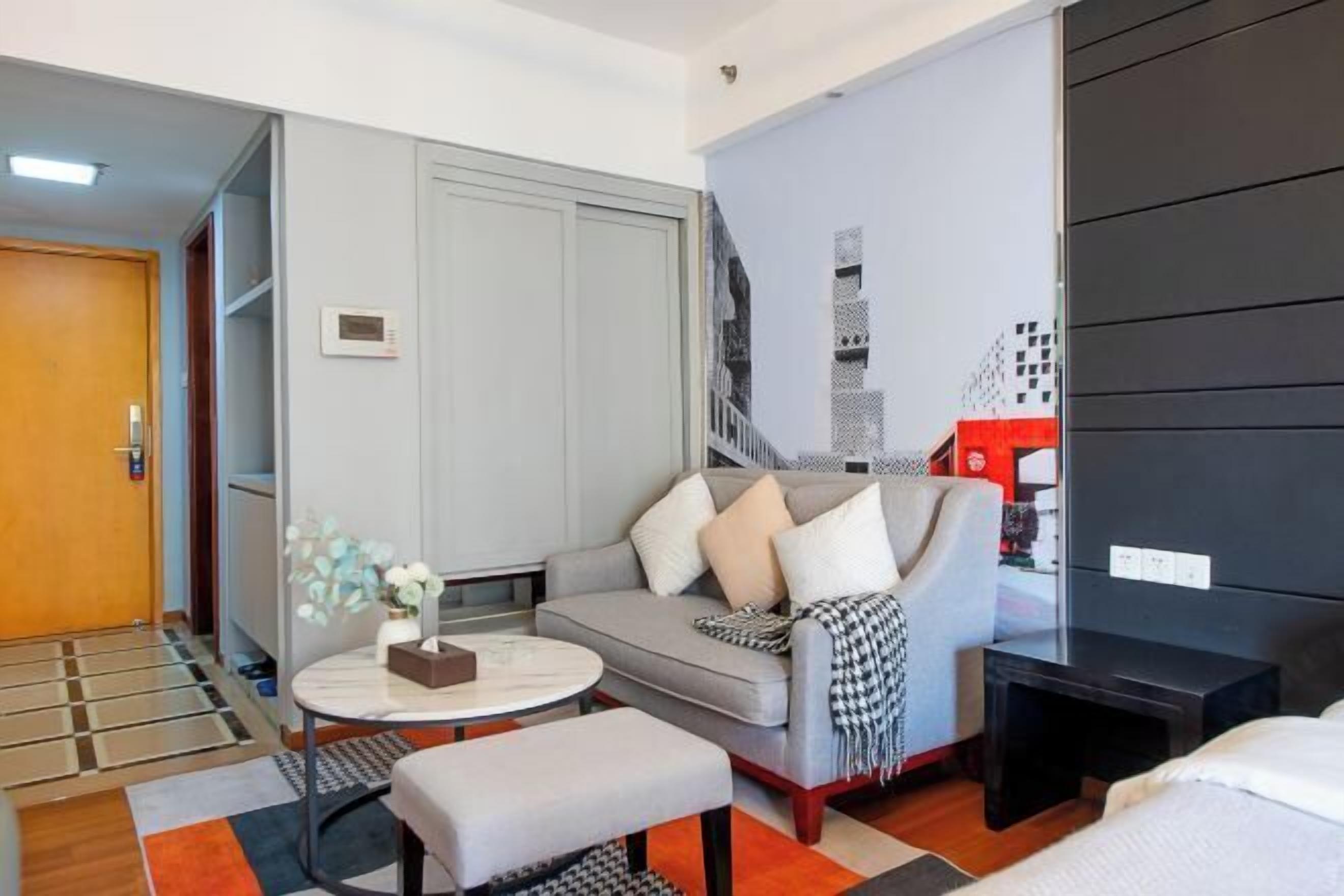 Ein modernes Hotelzimmer mit grauem Sofa, einem runden Couchtisch, einem kleinen Nachttisch, einem schwarzen Kleiderschrank und einer sichtbaren Treppe.
