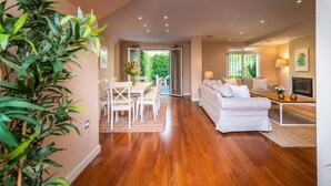 A spacious living area with a wooden floor, a white sofa, a dining table with chairs, and a view of the outdoors through a glass door. - Casa la Concha - Marbellamar (Marbella)