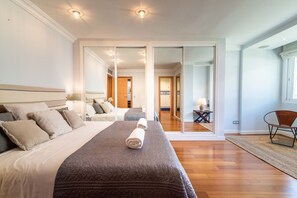 A hotel room with a large bed, a sliding glass door leading to a balcony, and a small table with a chair.