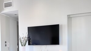 A modern living room with a flat-screen TV mounted on the wall, a wooden cabinet with a vase and candles, and a wooden floor. - La Terrasse in the heart of the old town. (Aix-en-Provence)