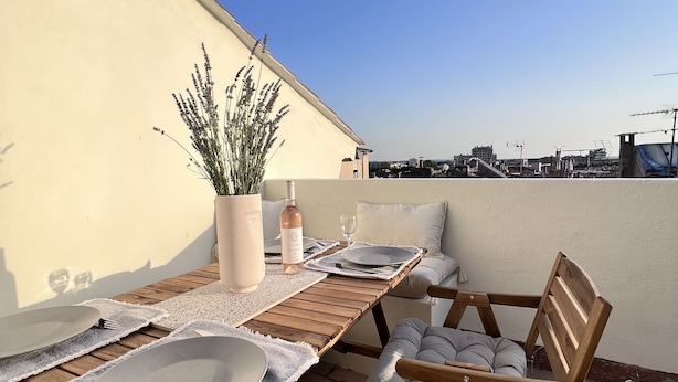 A rooftop terrace with a wooden table set for two, a cushioned chair, and a potted plant. - La Terrasse in the heart of the old town. (Aix-en-Provence)