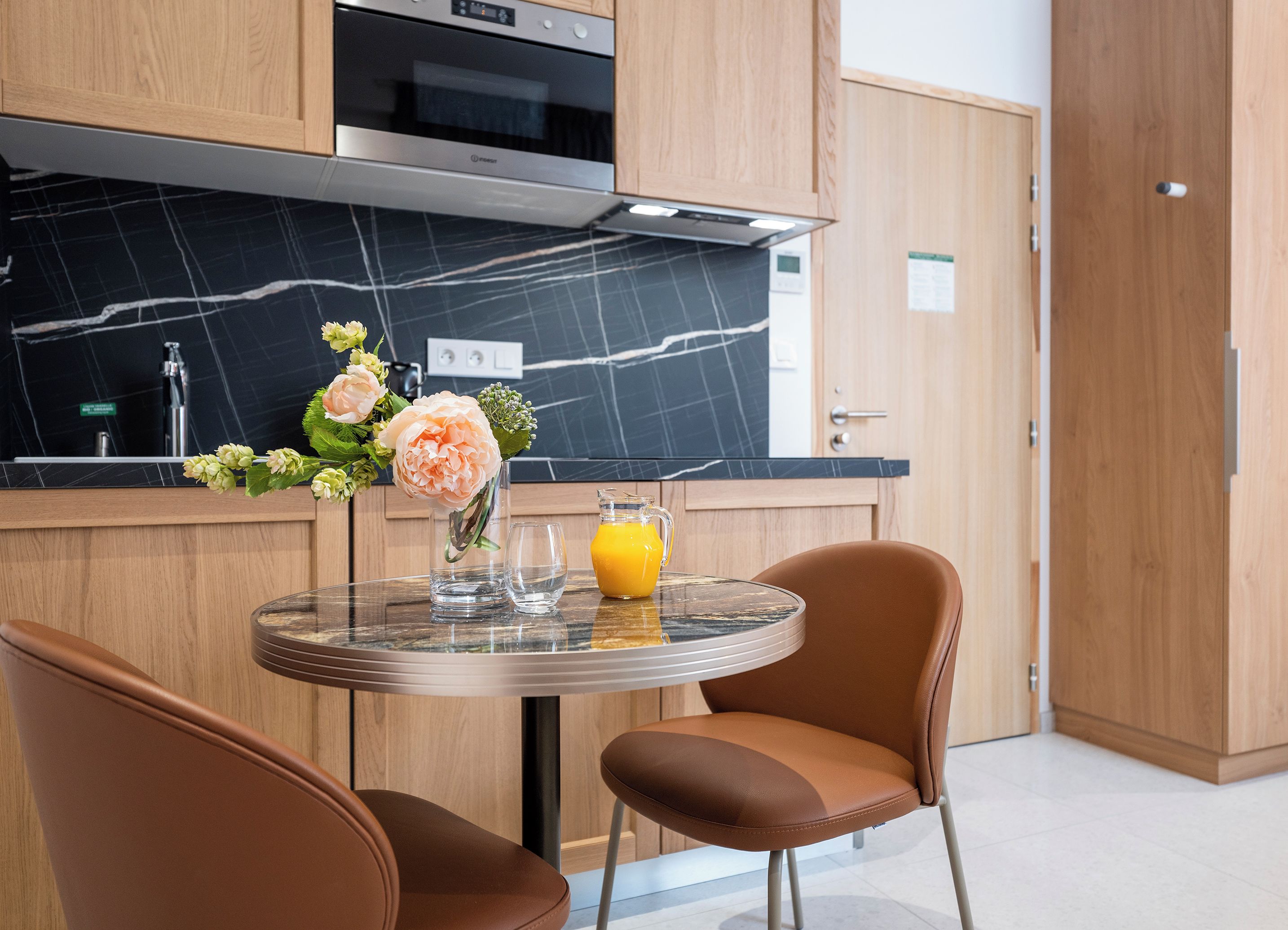 Una cocina moderna con horno empotrado, encimera de mármol y comedor con dos sillas y una mesa.