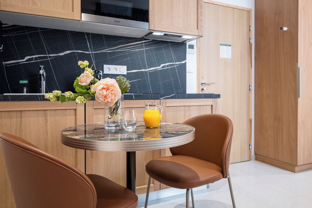 A modern kitchen with a built-in oven, a marble countertop, and a dining area with two chairs and a table.