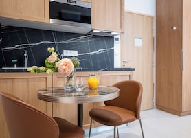 Une cuisine moderne dotée d’un four encastré, d’un plan de travail en marbre et d’un coin repas avec deux chaises et une table.