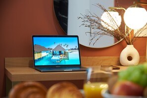 A laptop displaying a resort scene, a vase with branches, and a wooden table with a glass of orange juice.