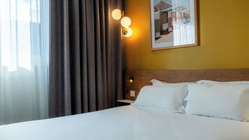 A hotel room with a bed, curtains, wall-mounted lights, and a framed picture.
