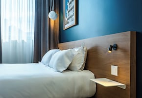 Une chambre d’hôtel avec un lit, une table de chevet, un tableau encadré au mur et une fenêtre avec des rideaux.