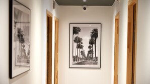 A hallway with framed artwork depicting palm trees and a street, wooden doors, and a ceiling light. - Corner Set (Cholet)