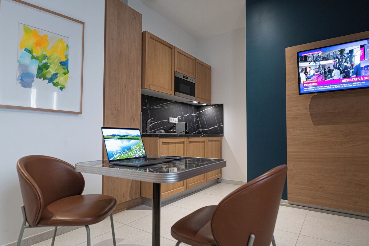 A modern kitchen with wooden cabinets, a black marble countertop, and a laptop on a glass table.