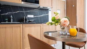 A modern kitchen with wooden cabinets, a marble countertop, and a dining area with a glass table and chairs. - Corner Set (Cholet)