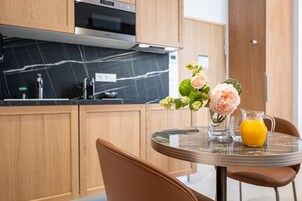 Une cuisine moderne avec des meubles en bois, un plan de travail en marbre et un coin repas comprenant une table et des chaises en verre.
